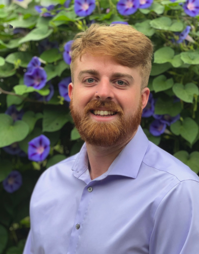blonde man in a lilac shirt, with purple flowers in the back_apartment finders