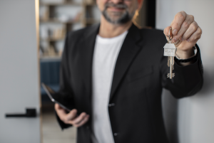 man with a black blazer and white t-shirt, showing the key with a silver home keychain_apartment insiders